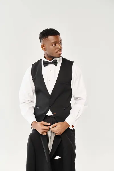 Handsome African American groom standing in a stylish tuxedo and bow tie against a grey background. — Stock Photo