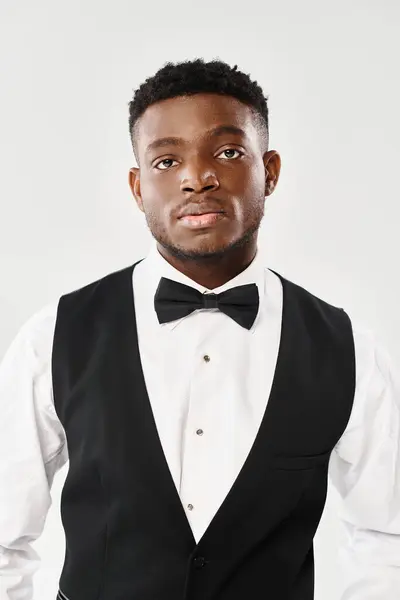 Young African American groom exudes style in a black vest and bow tie against a grey studio background. — Stock Photo