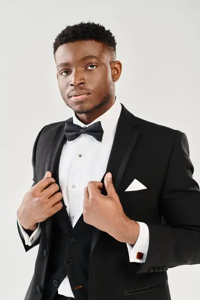 A young and handsome African American groom in a tuxedo striking a confident pose in a studio setting against a grey background. — Stock Photo