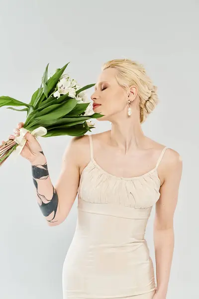 Une belle mariée blonde dans une robe de mariée tenant gracieusement un bouquet de fleurs colorées. — Photo de stock