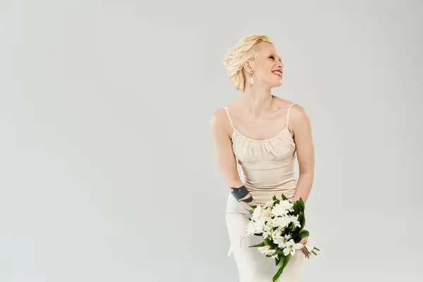 Une belle mariée blonde dans une robe de mariée tenant un bouquet de fleurs, exsudant sérénité et élégance. — Photo de stock