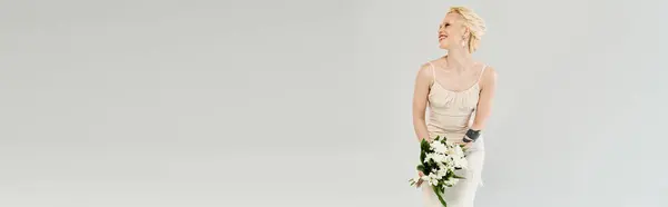 Une superbe mariée blonde se tient gracieusement dans une robe blanche, tenant délicatement un bouquet luxuriant de fleurs vibrantes. — Photo de stock