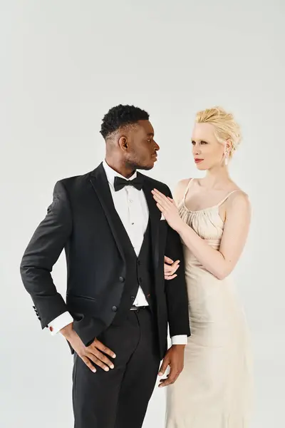 A beautiful blonde bride in a wedding dress and an African American groom in a tuxedo standing side by side. — Stock Photo