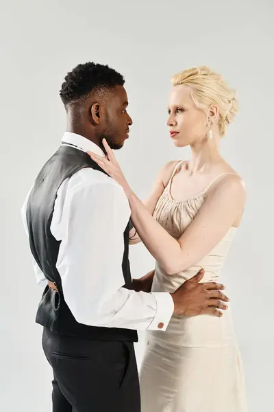 Uma noiva loira bonita em um vestido de noiva está lado a lado com um noivo afro-americano em um estúdio em um fundo cinza. — Fotografia de Stock