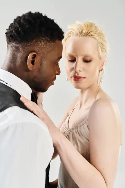 A beautiful blonde bride in a wedding dress standing next to an African American groom in a studio on a grey background. — Stock Photo