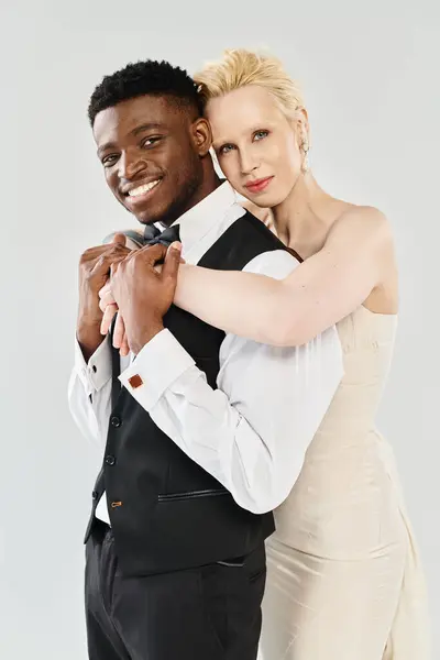 Uma noiva loira bonita em um vestido de noiva e um noivo afro-americano posando para um retrato em um estúdio em um fundo cinza. — Fotografia de Stock