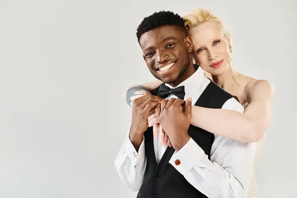 Un hombre elegante con esmoquin abraza tiernamente a una mujer con un elegante vestido blanco y negro. El amor y la sofisticación están en el aire. - foto de stock