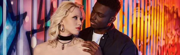 A blonde woman and African American man stand together in front of a vibrant, graffiti-covered wall on an urban street. — Stock Photo