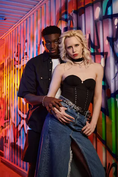A blonde woman and African American man stand side by side on an urban street with graffiti on walls. — Stock Photo