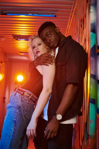 A blonde woman and an African American man stand side by side on an urban street with colorful graffiti on the walls. — Stock Photo