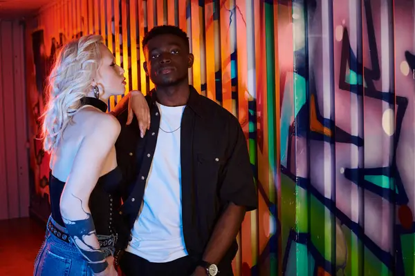 Блондинка и афроамериканец стоят перед красочной городской стеной, украшенной граффити.. — стоковое фото