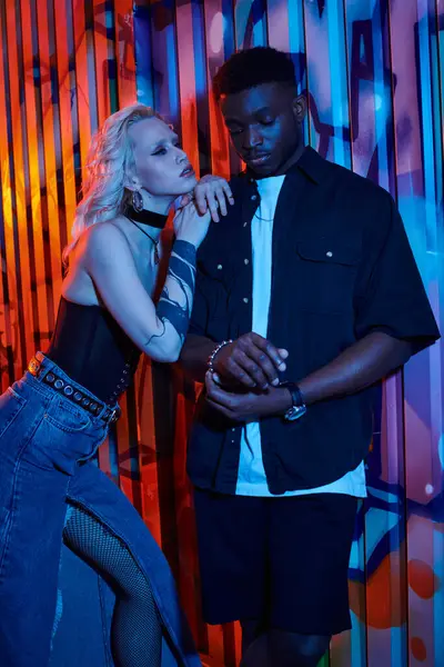 A blonde woman and an African American man stand side by side on an urban street with graffiti-covered walls. — Stock Photo