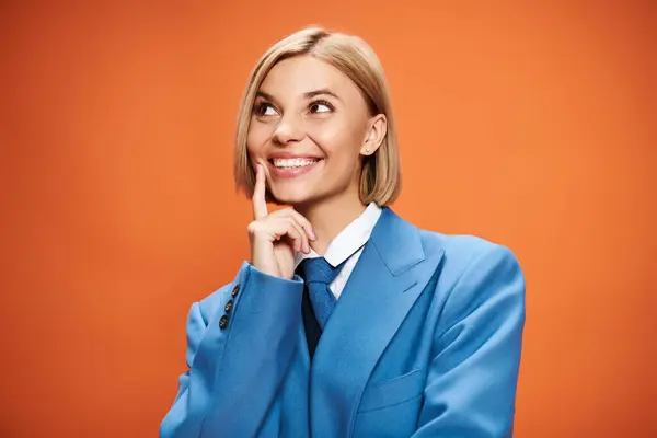 Mulher atraente alegre com cabelo loiro em traje elegante elegante posando em pano de fundo laranja — Fotografia de Stock