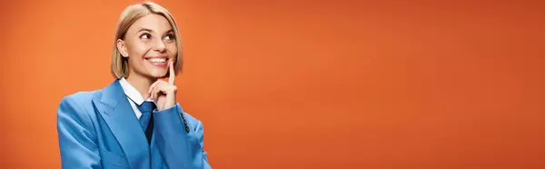 Happy sophisticated woman with blonde hair in elegant attire posing on orange backdrop, banner — Stock Photo