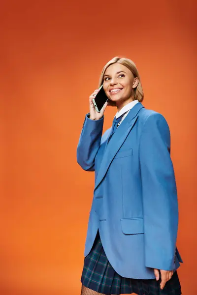 Joyous well dressed woman with short blonde hair in chic attire holding phone on orange backdrop — Stock Photo