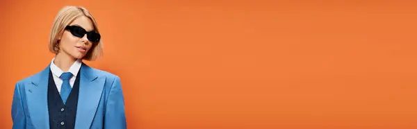 Beautiful woman with short hair in chic attire with sunglasses posing on orange backdrop, banner — Stock Photo