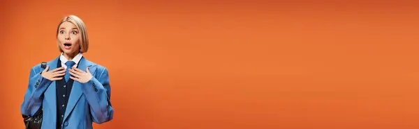 Shocked woman with short blonde hair in sophisticated attire posing on orange backdrop, banner — Stock Photo