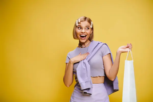 Positive appealing woman with accessories in chic attire posing with shopping bag on yellow backdrop — Stock Photo