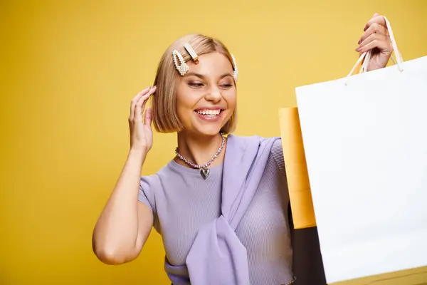Joyful good looking woman with short hair posing on yellow background with shopping bags in hands — Stock Photo