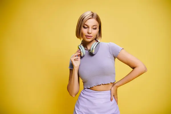 Delighted joyous woman with short blonde hair and headphones enjoying music on yellow backdrop — Stock Photo