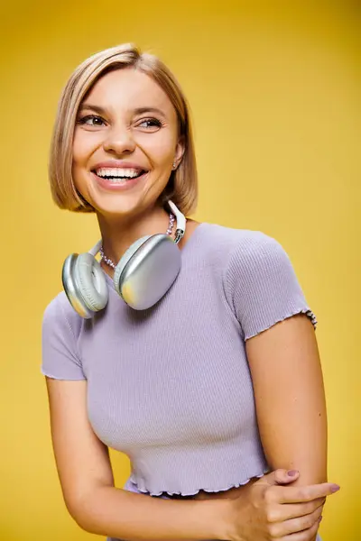 Pleased joyous woman with short blonde hair and headphones enjoying music on yellow backdrop — Stock Photo