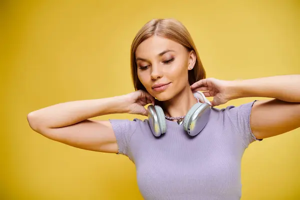 Mujer alegre emocionada con el pelo corto y rubio y auriculares disfrutando de la música en el fondo amarillo - foto de stock