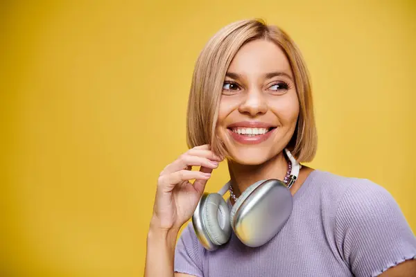Charming joyous woman with short blonde hair and headphones enjoying music on yellow backdrop — Stock Photo