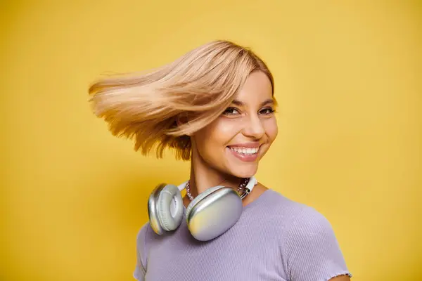 Mujer alegre refinada con pelo corto y rubio y auriculares disfrutando de la música en el fondo amarillo - foto de stock
