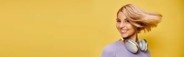 Chic joyous woman with short blonde hair and headphones enjoying music on yellow backdrop, banner — Stock Photo