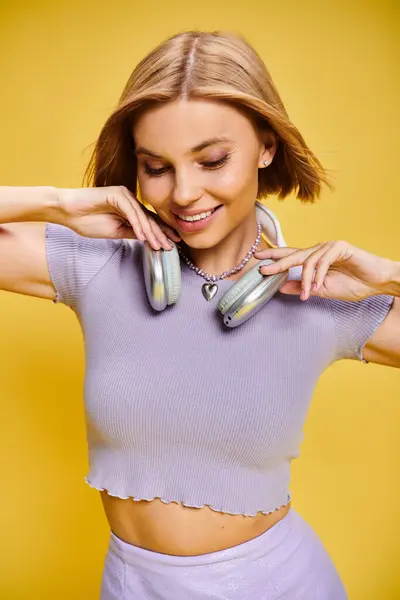 Elegant joyous woman with short blonde hair and headphones enjoying music on yellow backdrop — Stock Photo