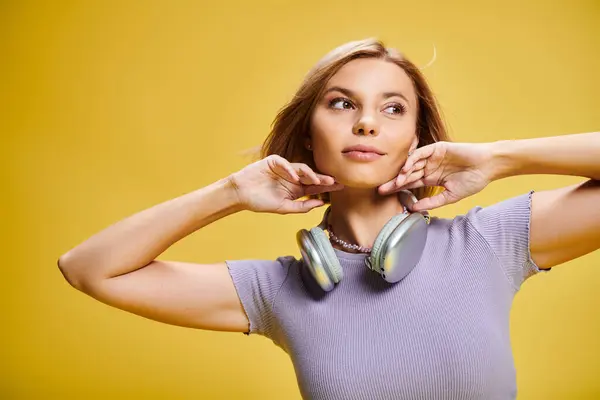 Hermosa mujer alegre con pelo corto y rubio y auriculares disfrutando de la música en el fondo amarillo - foto de stock