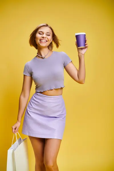 Joyous young woman in vibrant attire with short hair posing with coffee and shopping bag in hands — Stock Photo