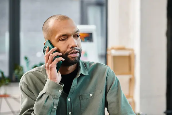 Un hombre discapacitado con miastenia grave en una camisa verde se involucra en una llamada telefónica en un entorno corporativo. - foto de stock