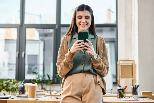 Профессиональная женщина стоит в современном офисе, поглощенная своим мобильным телефоном. — стоковое фото