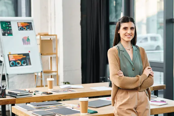 Жінка впевнено стоїть перед столом у корпоративному офісі, втілюючи лідерство і творчість. — стокове фото