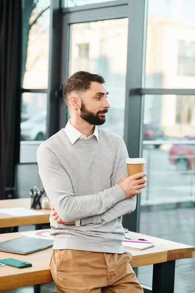 A man is seated at a table, quietly enjoying a cup of coffee in a modern office setting. — Stock Photo