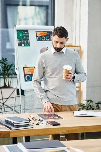 A man relaxes at a table with a cup of coffee in a bustling office environment, taking a moment to regroup amidst corporate hustle. — Photo de stock
