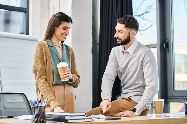 A man and woman collaborate on a project at a desk, taking a break with coffee in a corporate office setting. — Stock Photo