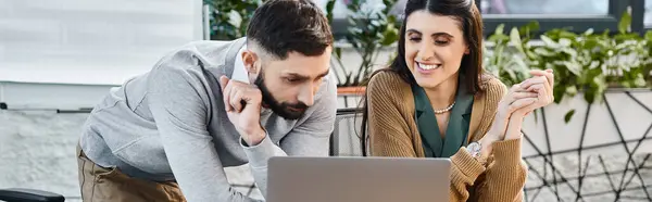 Un hombre y una mujer trabajan en un ordenador portátil en un entorno de oficina corporativa, unidos en su enfoque y determinación. - foto de stock
