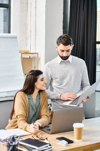 A man and woman engage in a coworking session, sitting at a table with a laptop, discussing a project in a corporate office setting. — Stock Photo