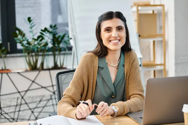 Eine arbeitswütige Frau sitzt vor ihrem Laptop in einem geschäftigen Büroumfeld. — Stockfoto