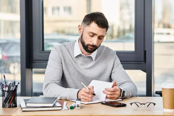 Человек в корпоративном офисе усердно пишет на клочке бумаги за своим столом, погруженный в мир слов. — стоковое фото