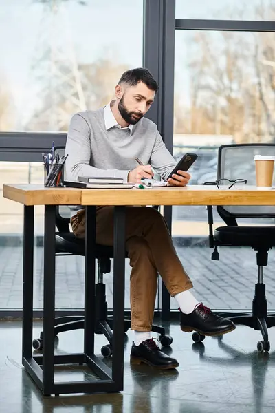Un hombre inmerso en su teléfono celular en una mesa en un entorno de oficina, parte de una cultura corporativa. - foto de stock