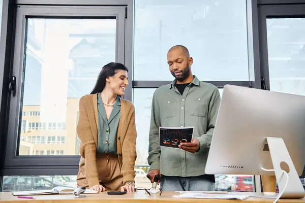 A man and a woman collaborate in an office, standing in front of a computer, working on a business project together. — Stock Photo