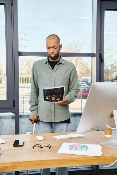 Un hombre se para con confianza frente a un escritorio, sosteniendo un libro mientras se prepara para un día productivo de trabajo en un entorno de oficina. - foto de stock