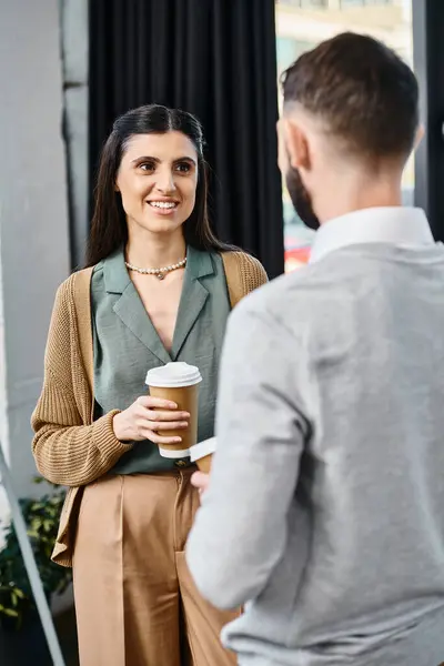 A woman and a man chatting casually while he holds a cup of coffee in an office setting. — Stock Photo