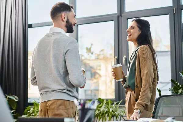 A man and a woman engage in a lively discussion in a modern office setting, reflecting the essence of teamwork in corporate culture. — Photo de stock