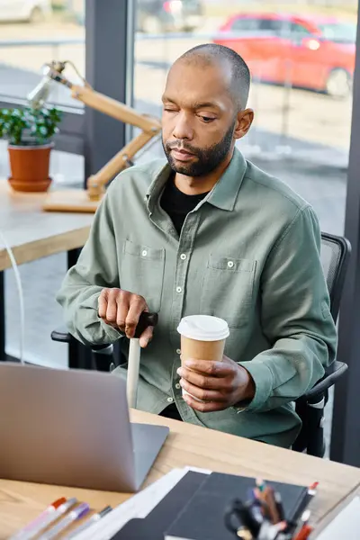Un hombre enfocado en su portátil mientras disfruta de una taza de café en una mesa en un entorno corporativo. - foto de stock