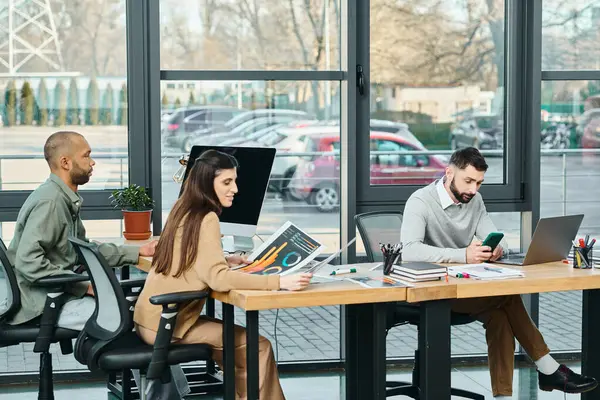 Tres profesionales sentados en una mesa en una oficina, cada uno absorto en sus computadoras portátiles, trabajando en un proyecto. - foto de stock