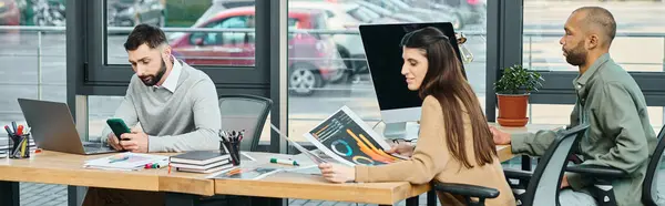 Un hombre y una mujer sentados en una mesa, cada uno centrado en las pantallas de sus portátiles, trabajando diligentemente en un proyecto en un entorno de oficina corporativa. - foto de stock